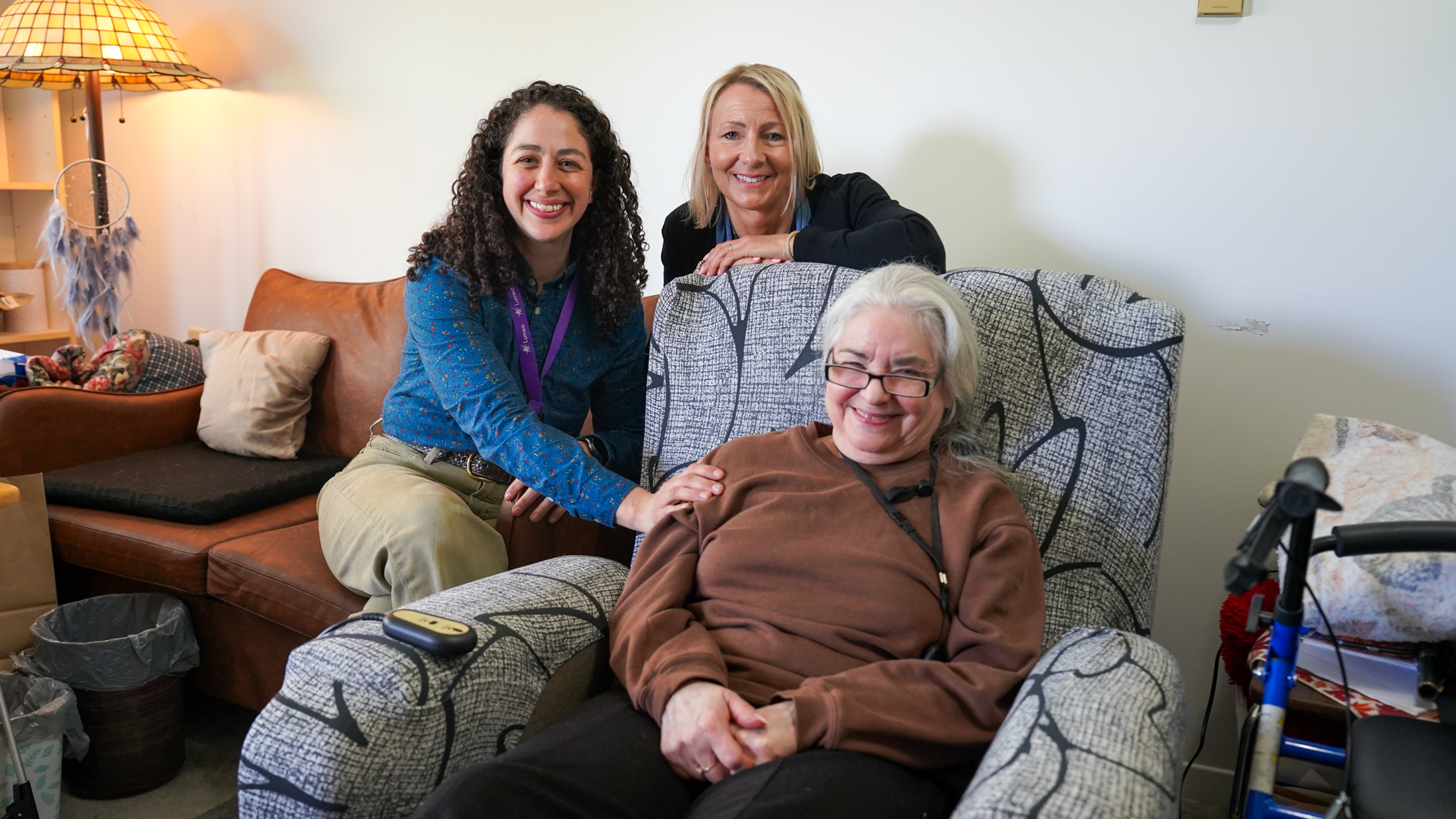 Community Rehabilitation Counselor Ames Findley [left] sits with Brockville CBIS Service Coordinator Laurie Ogilvie [back] and client Dawn Pyke in her home with her new recliner.